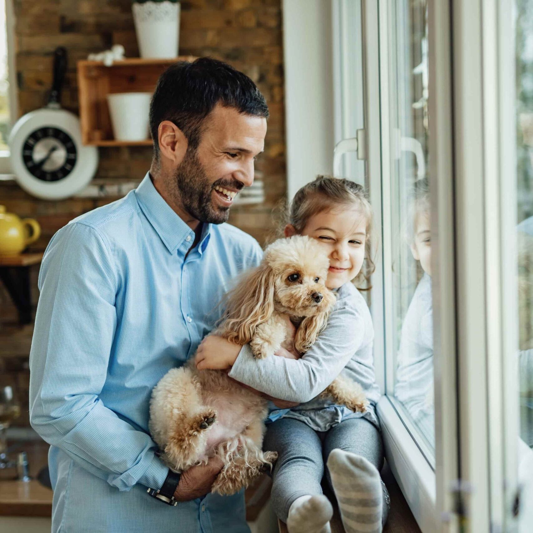 Vader en dochter kijken door een groot raam, houden een hond vast en genieten van het uitzicht.