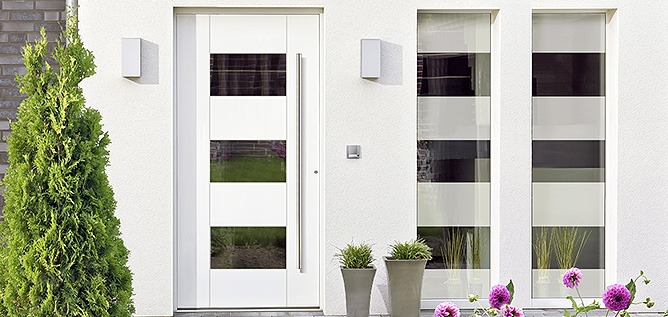 Moderne witte voordeur met glazen stroken, geflankeerd door smalle ramen, minimalistische buitenlampen en decoratieve planten.