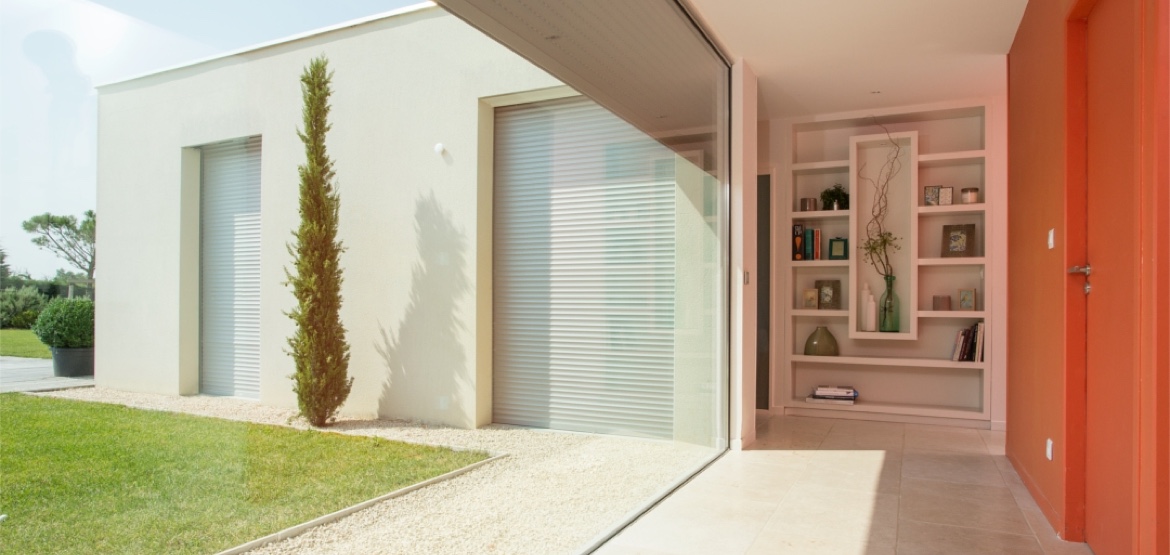 Modern huis met lichte gevel, grote glaspartijen, een boekenkast en een kleurrijke wand in het interieur.