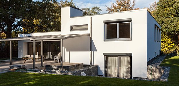 Modern tweeverdiepingshuis met plat dak, grote ramen, terras en omgeven door een groene tuin.