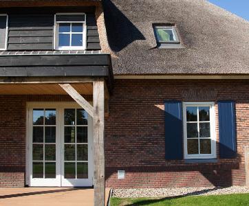 ChatGPT: ChatGPT Traditioneel bakstenen huis met rieten dak, roedenramen en dubbele vleugeldeur, omgeven door een groene tuin.