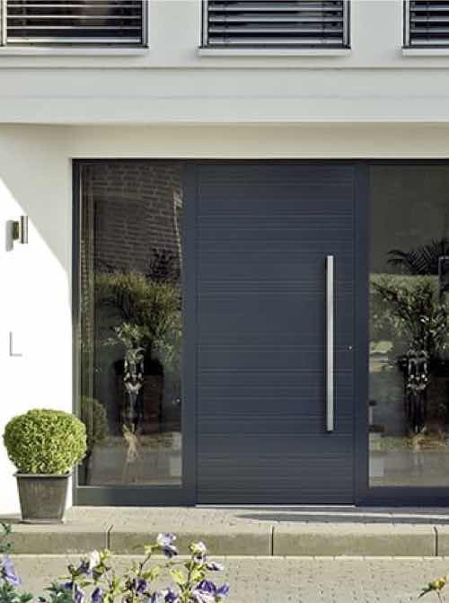 Moderne voordeur in antraciet met glaselementen, omgeven door een witte gevel en decoratieve planten.
