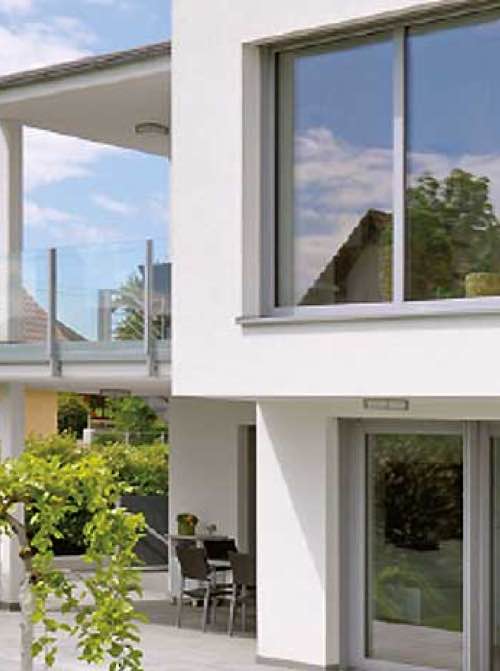 Modern wit huis met grote glazen ramen, een balkon met glazen balustrade en een groene tuin.