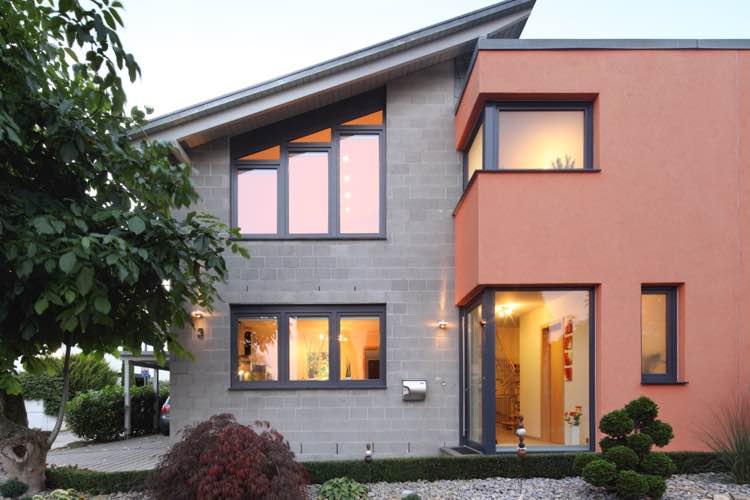 Modern vrijstaand huis met grote, grijze kunststoframen, deels gestuukt in oranje, en een gestructureerde betongevel.