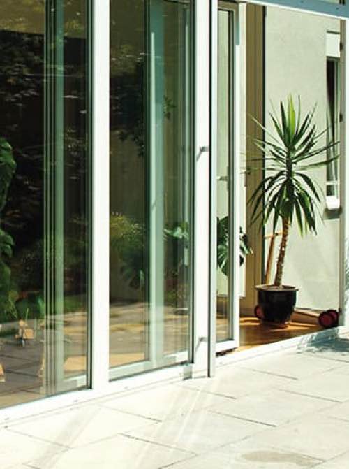 Moderne glazen schuifdeuren met een wit frame, die een zonnige toegang tot een tuin of binnenplaats bieden.